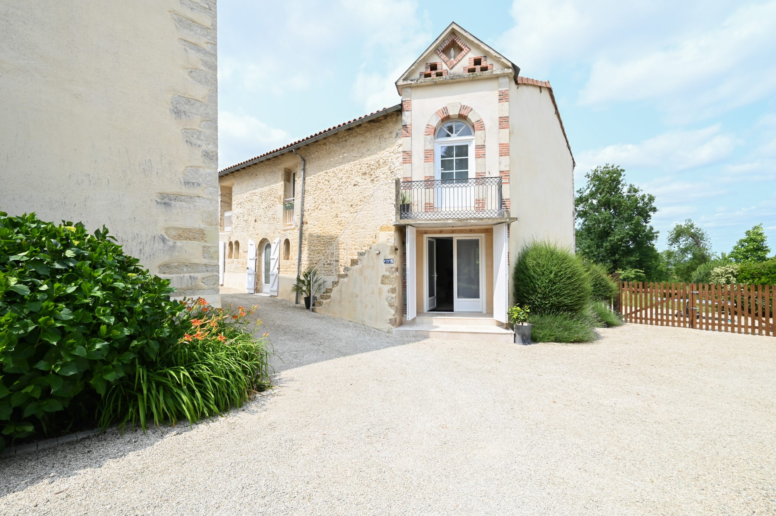 Charming Vendee Gite, view across gravel path to the stone frontage of the vendee gite with tower and shrubs at the side of the house